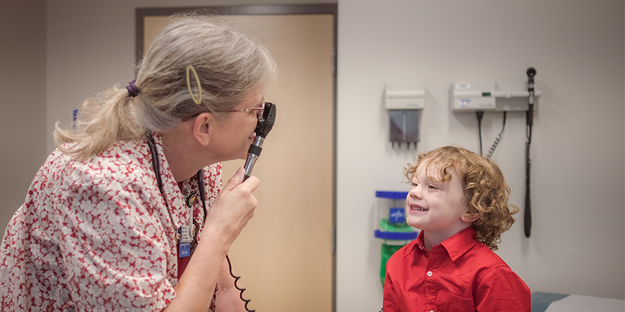 pip-PrimaryCare_Minnetonka-0475 copy A doctor examines a young child with curly hair sitting on bed at a clinic.